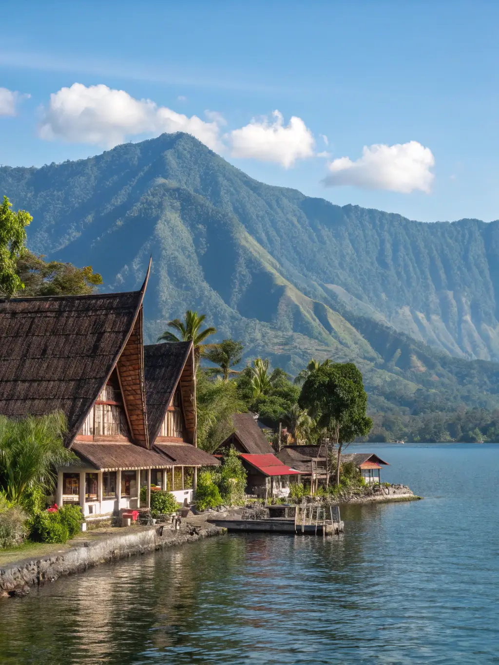 A serene image of Lake Toba in Sumatra, with traditional Batak houses along the shoreline and the surrounding mountains reflected in the calm waters.